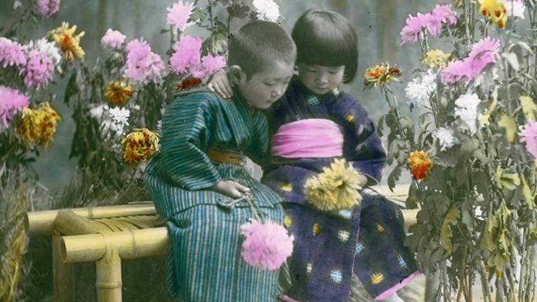 Two children sitting on a bench in kimono outfit with pastel pink, yellow and white flowers