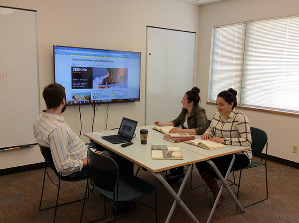 Three people sitting at a table in front of a televsion monitor