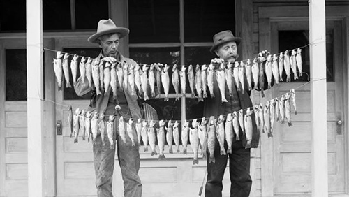 Historical photo of two men holding a strings of fish between them