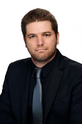 A male-presenting person with light skin tone and short dark hair, wearing a black business shirt and grey tie. 