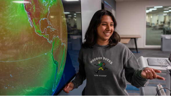 A college student presents in front of a large projected image of the earth.