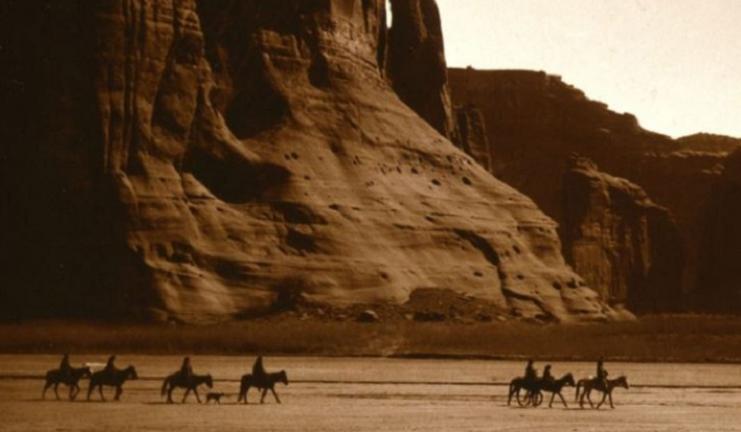Sepia tone photo of Native Americans riding horses in desert southwest landscape