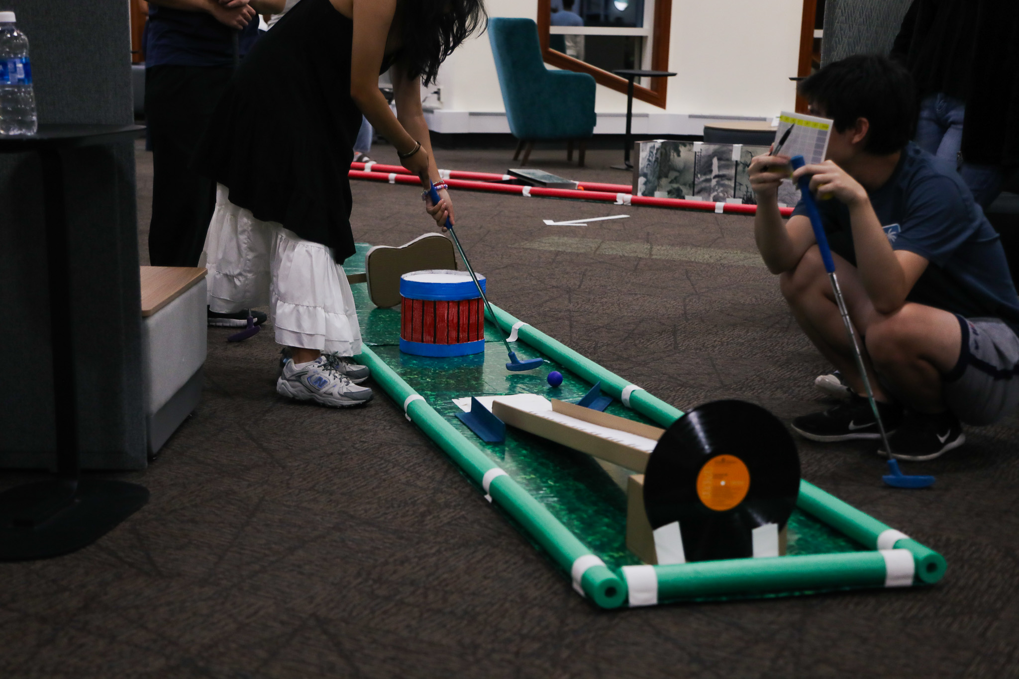 A student putting a golf ball on a music-themed hole of the indoor mini-golf course.
