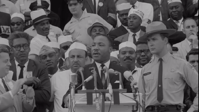 Dr. Martin Luther King, Jr. at a podium surrounded by a crowd