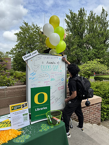 A student writing on a whiteboard outside Knight Library entrance.