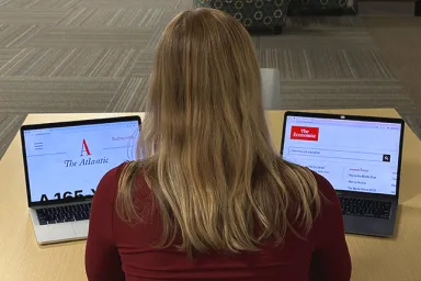 A library visotor with her back to the viewer looks at two laptops with the Atlantic and Economist magazines sites on the screens.