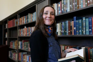 Emily Moore holding an open book, standing next to a bookcase in Special Collections.