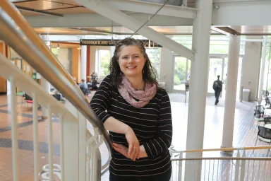Genifer Snipes leaning on the stairway railing in the atrium of the Lillis Business Complex