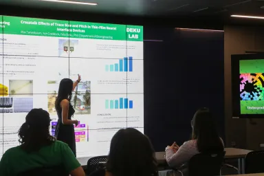 A student pointing to slide with research graphics on the VizLab display screen.