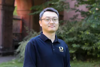Le Yang standing in front of Knight Library with red brick and green foliage in background.