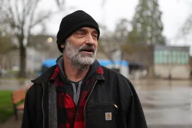 Tim Lewis wearing a beanie hat, standing on a rainy street in Eugene