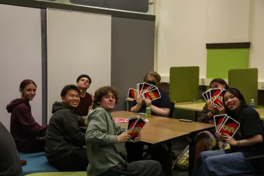 Diverse group of male and female students playing UNO card game at a library table.