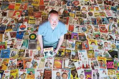 the first 200 issues of MAD magazine spread out on a floor with collector and donor Doug Gilford crouching at the center.