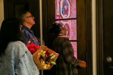 Three people looking into phone booth housing Tiny galleries exhibit; one is holding a bouquet of flowers.
