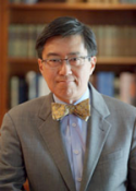 Brian Lym in suit and bow tie in front of bookcase