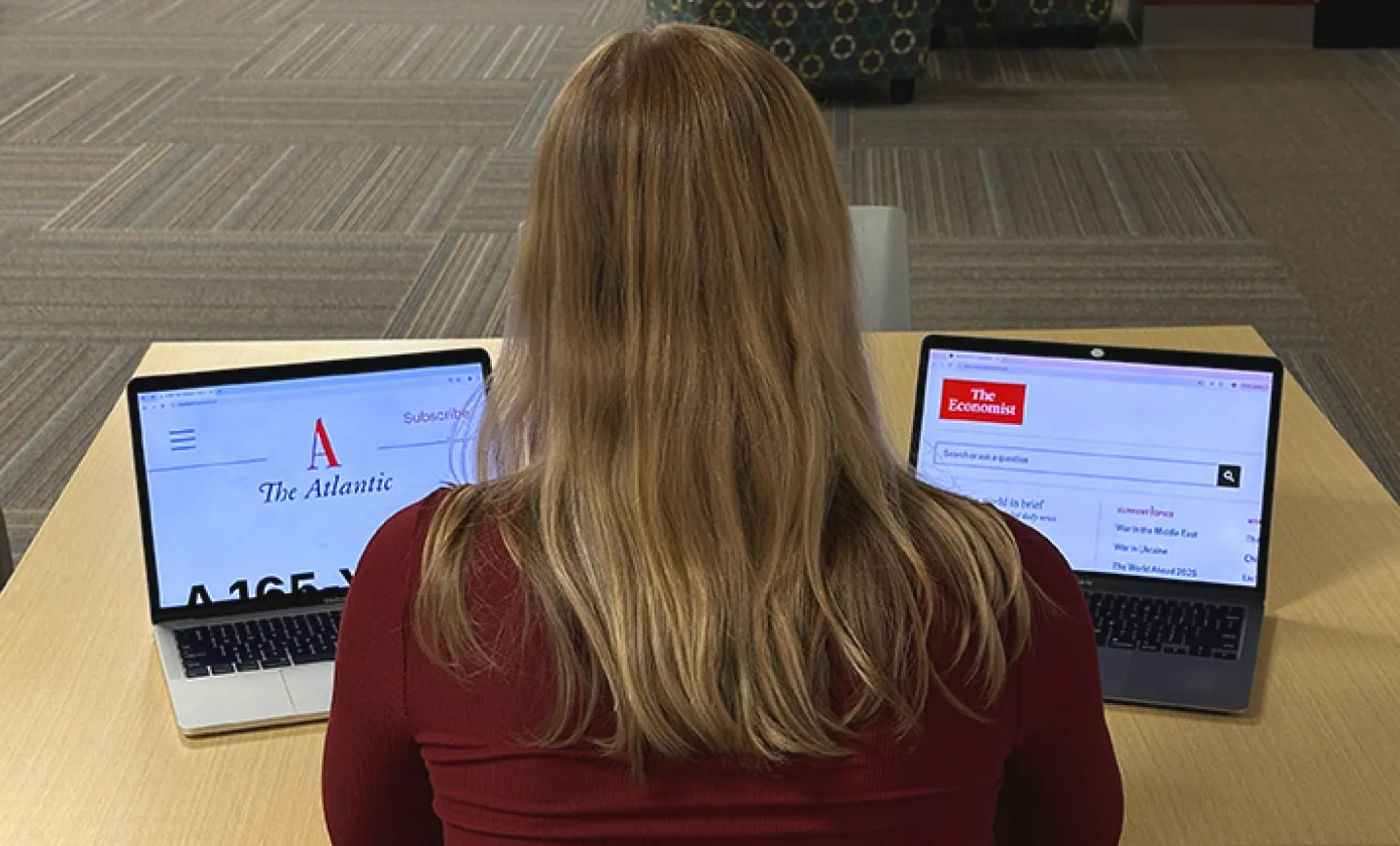 A library visotor with her back to the viewer looks at two laptops with the Atlantic and Economist magazines sites on the screens.