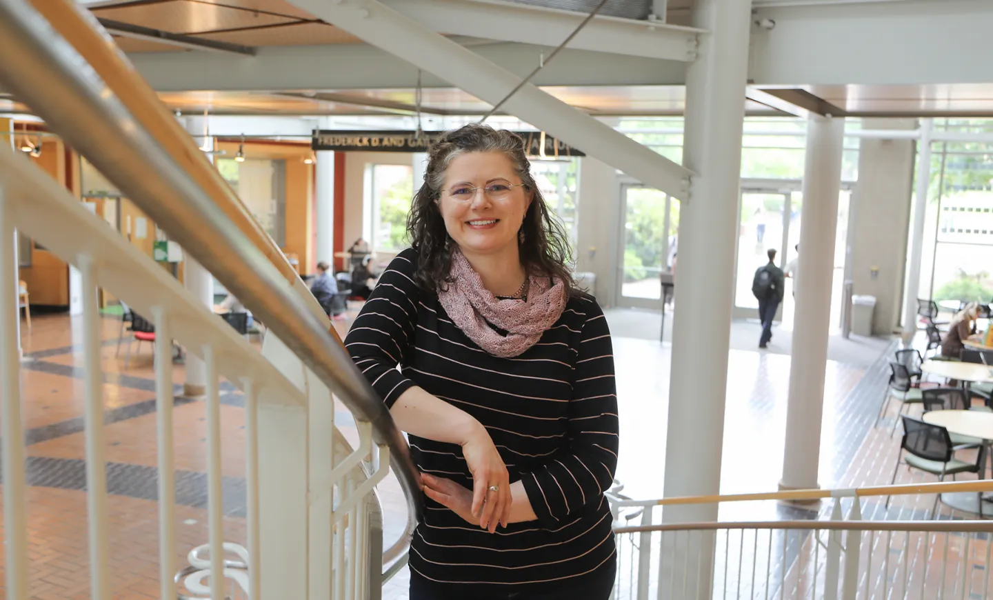 Genifer Snipes leaning on the stairway railing in the atrium of the Lillis Business Complex