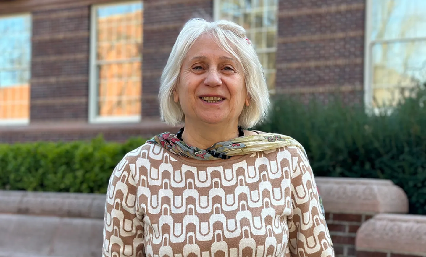 Portrait photo of Heghine Hakobyan standing outside Knight Library. She is wearing a patterned sweater and scarf.