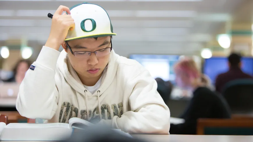 A student with a baseball cap scratching his head and studying