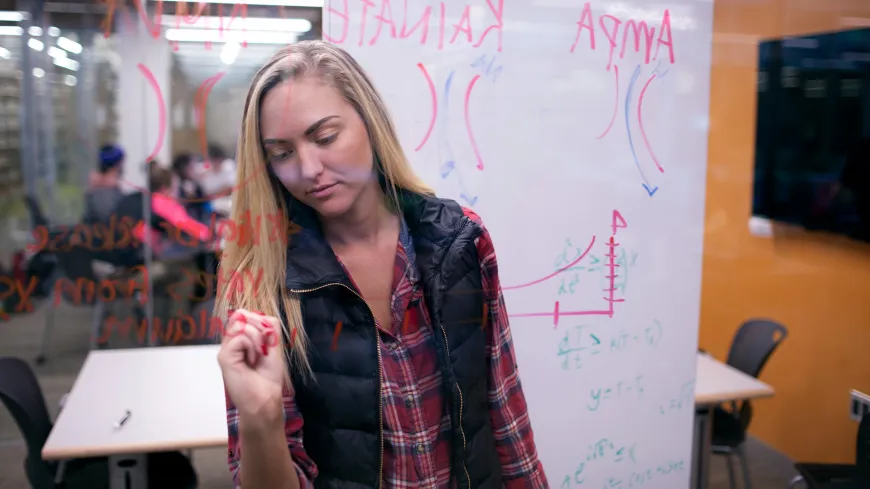 student writing on glass in front of a white board