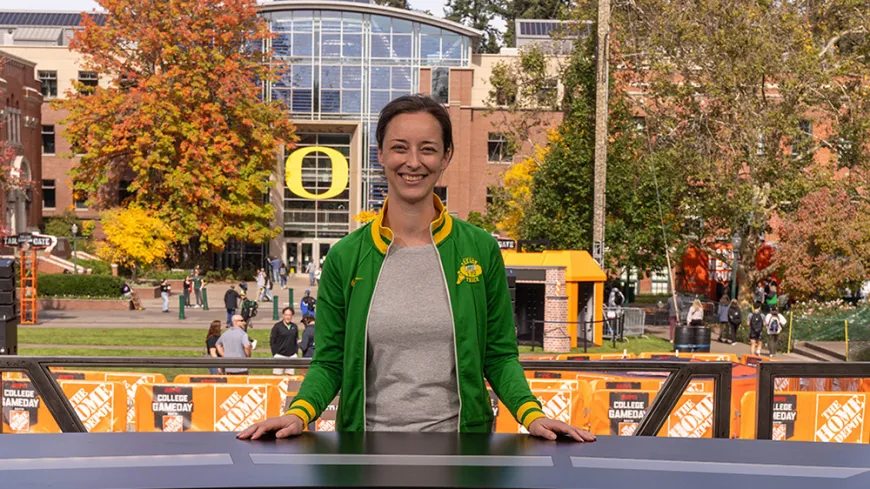 person outside at news desk with trees and buildings behind her