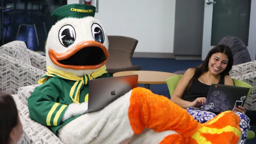 Duck mascot and student sitting and looking at laptops