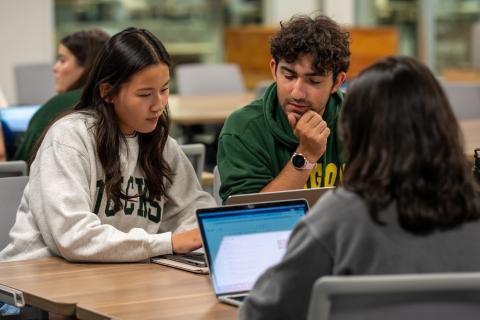 Three students sitting at a table looking at laptops