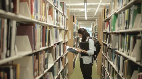 woman reading a book in the library stacks at PSC