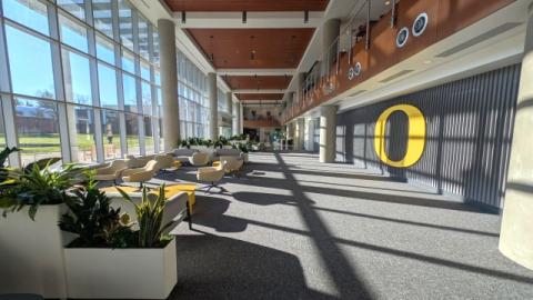 Open lobby of the Portland Library building with large windows, lounge seating, plants and event space exterior with a large yellow UO logo