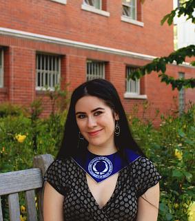 Kayla Kuo sitting on a campus bench, wearing a graduation sash.