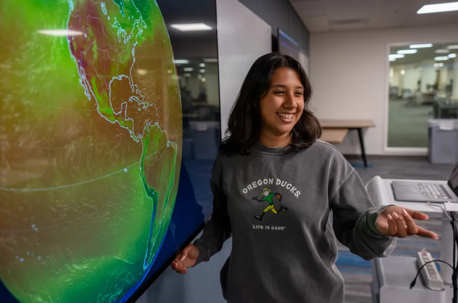 A student standing in front of a screen with an image of Earth on it