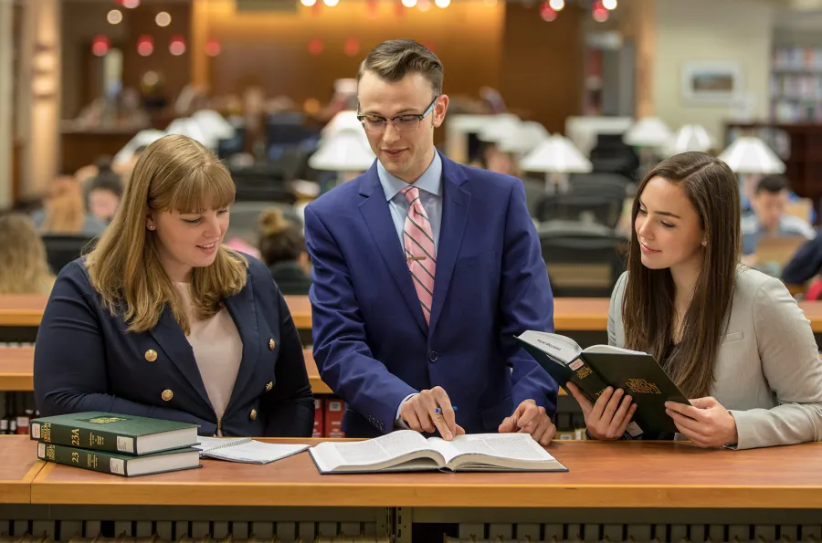 three law students standing at a shelf looking at books