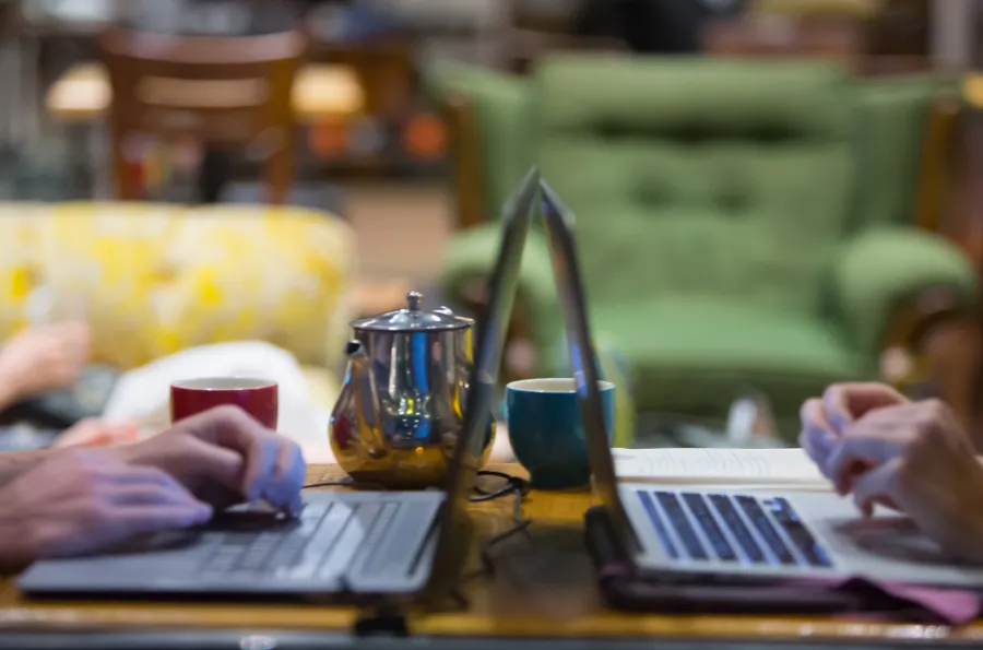 two laptops open with a teapot in the background