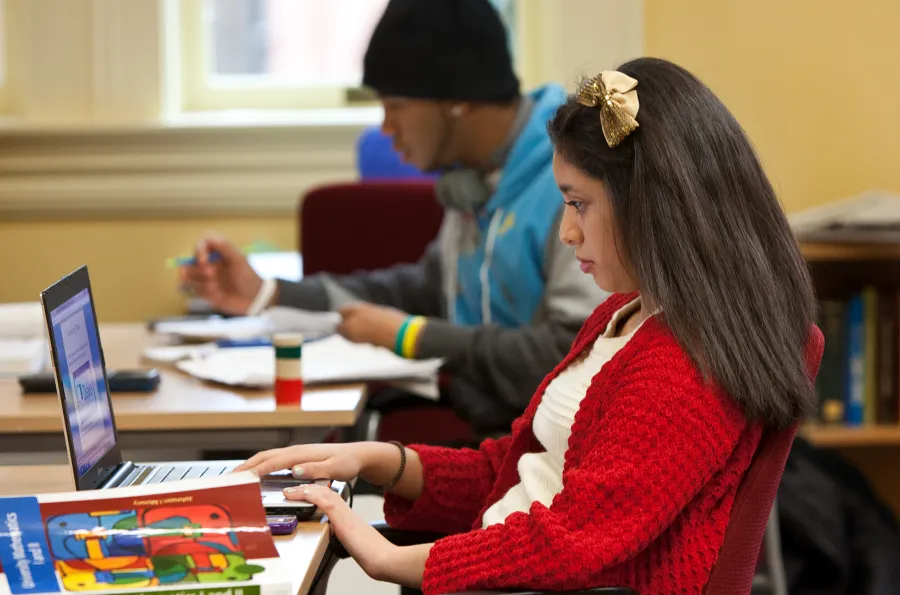 Two students looking at a laptop and textbooks