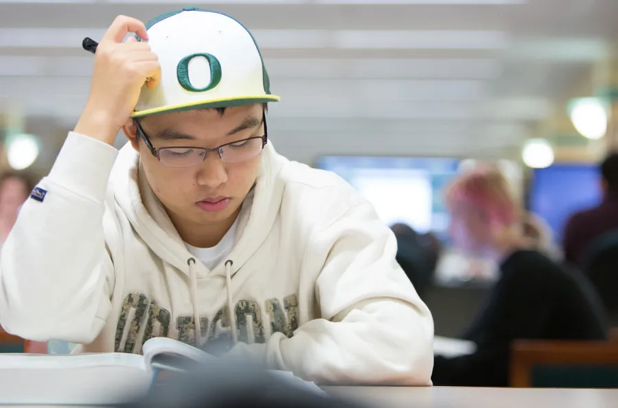 A student with a baseball cap scratching his head and studying