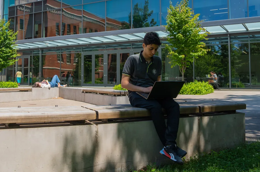 a person sitting on a cement wall outside looking at a laptop