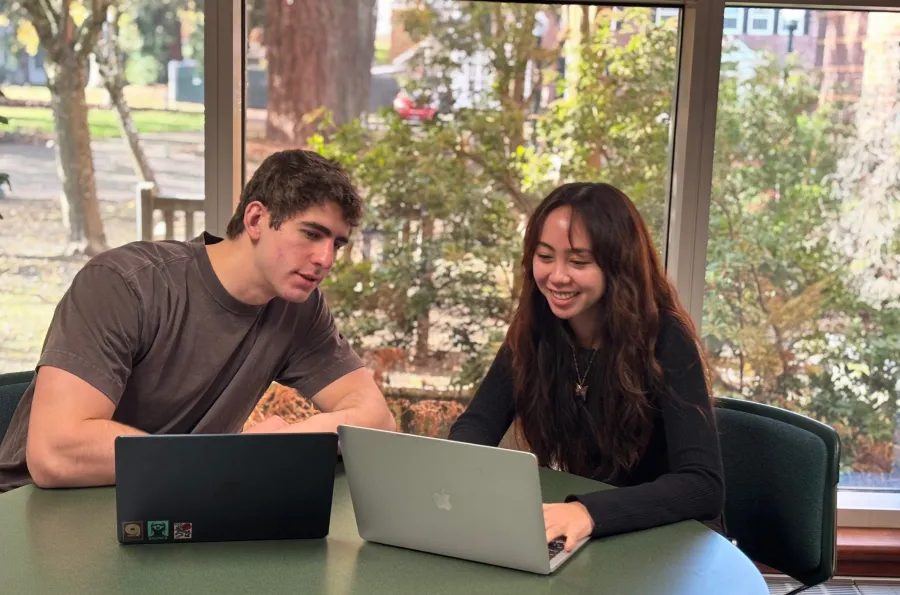 A tutoring session with two peers at a table with a window background.