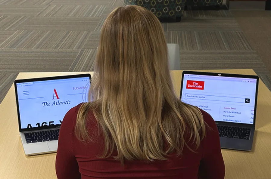 A library visotor with her back to the viewer looks at two laptops with the Atlantic and Economist magazines sites on the screens.