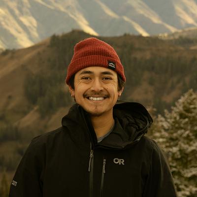 Freddy Lopez wearing a red beanie hat; mountains are visible in background.